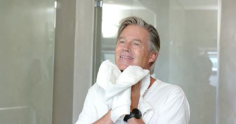 Mature man patting face with towel in bathroom mirror grooming skincare routine