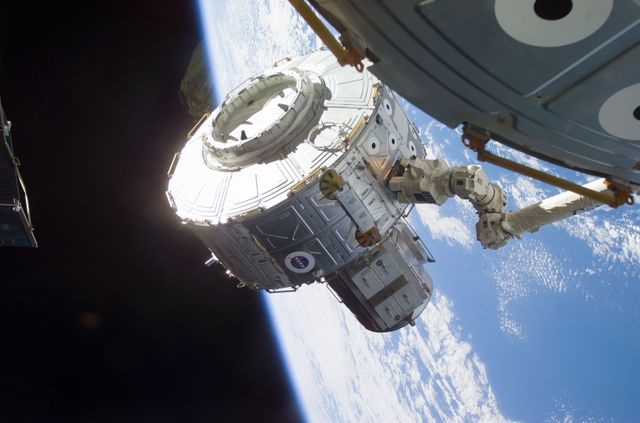 Quest Airlock being installed on the International Space Station using the Canadarm2 with Earth in background, taken July 2001. Ideal for illustrating space exploration, ISS operations, international cooperation in space, technology, engineering, NASA achievements, and historical space imagery.