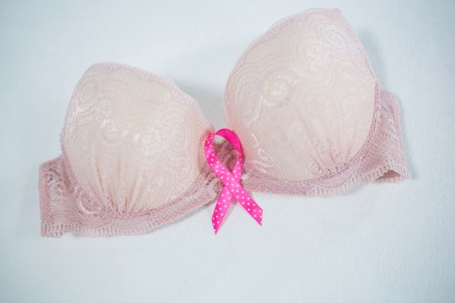 High angle view of spotted pink Breast Cancer ribbon on bra against white background
