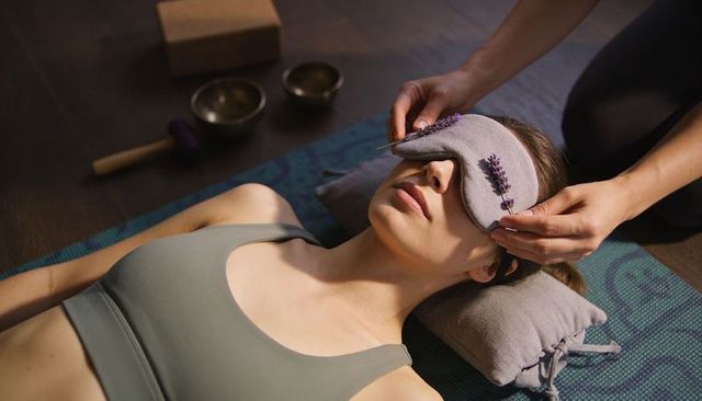 Woman receiving relaxing aromatherapy eye mask treatment with lavender and singing bowls