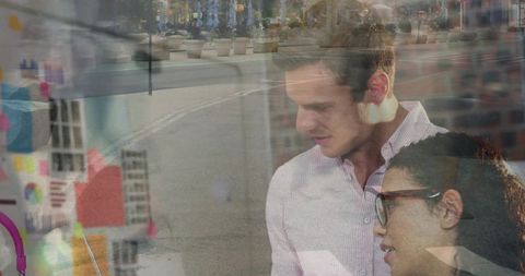 Professionals collaborating over tablet in storefront with sticky notes and reflections