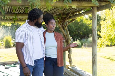 African american couple standing under pergola, talking and embracing in sunlit garden