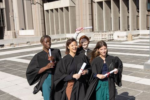 Diverse female graduates walking across university plaza holding diplomas and smiling
