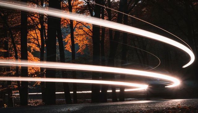 Spiraling light trails weaving through autumn forest along winding road at dusk