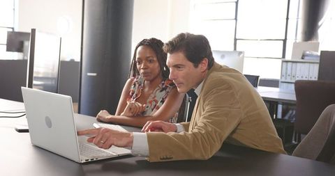 Colleagues collaborating on office desk with laptop discussion