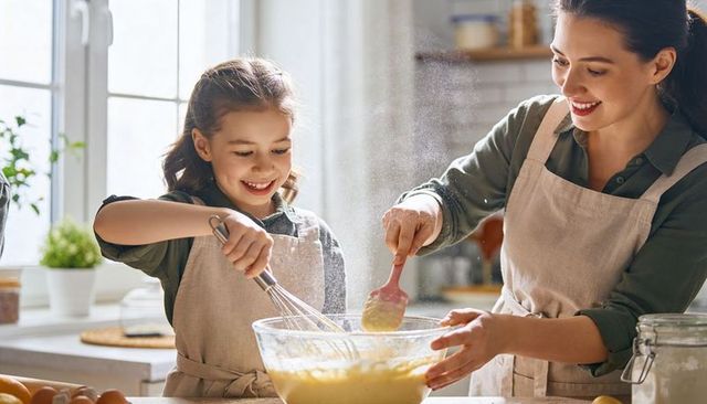 Mother and daughter baking together in bright kitchen mixing batter and laughing