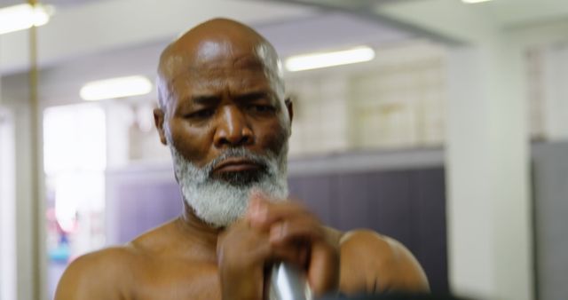 An elderly man lifting weights in a gym, demonstrating strength and determination in his fitness routine. This image can be used in articles or advertisements related to senior fitness, health programs, inspirational fitness journeys, and promoting healthy lifestyles for older adults.