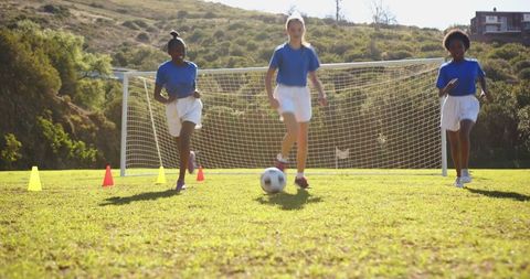 Diverse Kids Playing Soccer on Field with Goal and Training Cones
