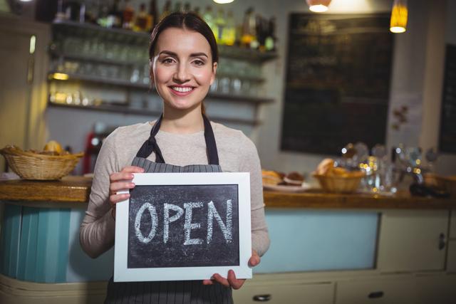Portrait of smiling waitress showing slate with open sign in cafÃ©
