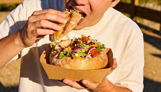 Man eating rustic bread bowl salad at outdoor picnic holding loaf bowl with fresh greens