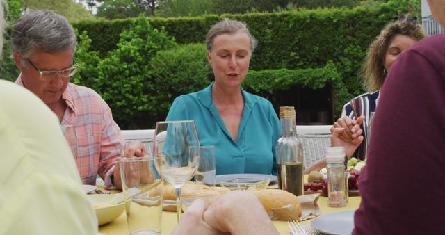 Image of happy diverse female and male senior friends having lunch in garden, praying. retirement lifestyle, spending quality time with friends.
