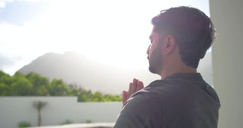 Adult indian man praying on balcony at sunrise, meditating for calm and mindfulness