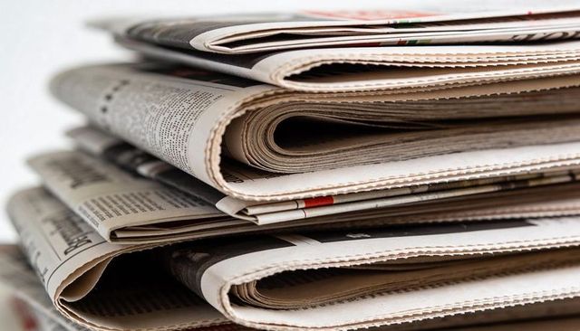 Stacked folded newspapers with visible headlines and textured pages for editorial use