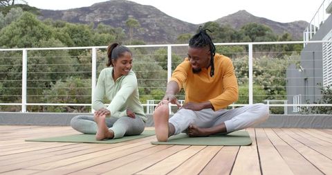 Asian and African American couple stretching on rooftop yoga mats overlooking mountains