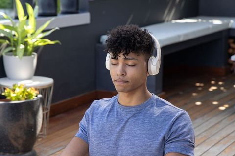 African american man meditating with headphones on sunlit terrace for mindfulness wellness