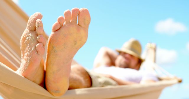 Close up of feet of caucasian man lying in hammock on beach. Summer, relaxation, leisure, vacation and lifestyle, unaltered.