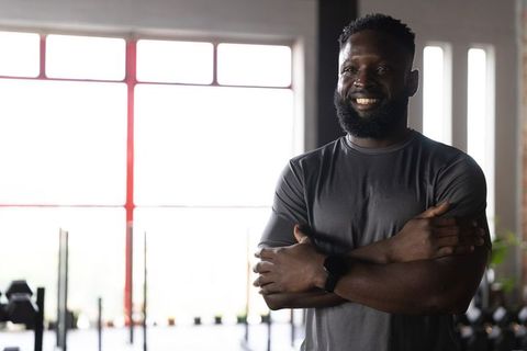 Confident african american trainer smiling with folded arms in bright gym muscular bearded smartwatc