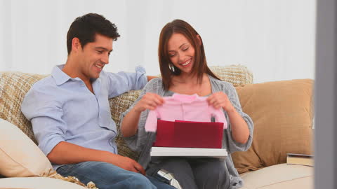 Expecting Couple Happy with Baby Outfit at Home
