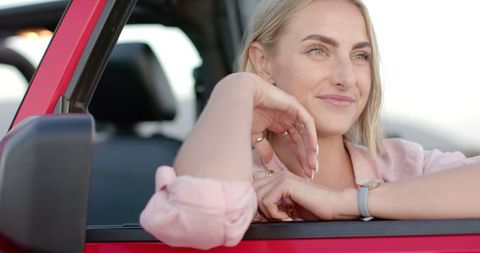 Blonde woman relaxing in red car on a scenic road trip
