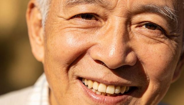 Smiling senior asian man showing warm teeth and crow's feet in golden-hour closeup
