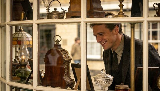 Smiling man browsing antique clocks and oil lamps through vintage shop window display