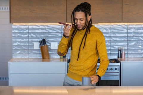 African american man speaking on phone while holding coffee mug at modern kitchen counter