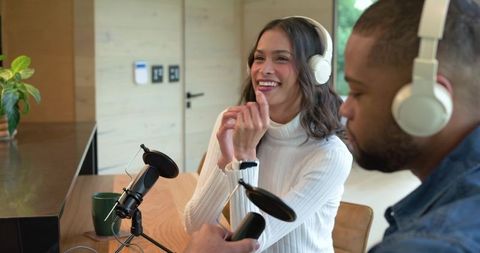 Diverse co-hosts recording lively home podcast at kitchen table with microphones and white headphone
