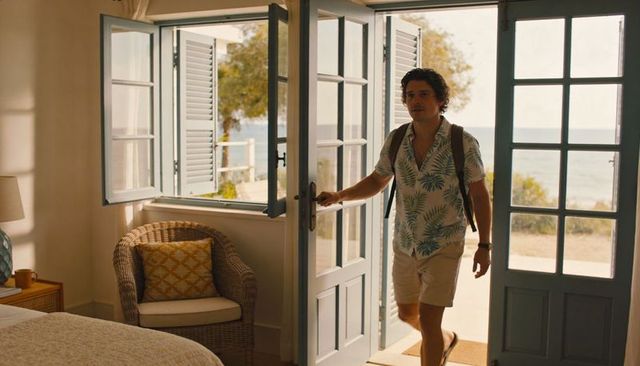 Traveler entering sunlit seaside cottage bedroom through blue french doors, tropical shirt and backp