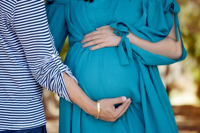 Expectant mother in a blue dress and partner in a striped shirt embracing her baby bump. This image is ideal for use in parenting, maternity, and family support contexts, as well as promotional materials for pregnancy-related products or services.