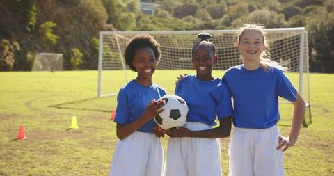 Diverse young girls smiling holding soccer ball on sunny field