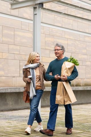 Senior couple walking through urban plaza carrying grocery bags and coffee