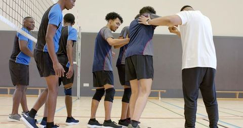 Diverse male volleyball team lining up at net during indoor practice