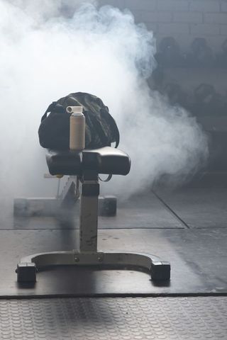 Moody gym bench with camouflage bag and water bottle in smoky industrial interior