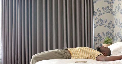 Person Relaxing on Bed Wearing Striped T-Shirt Beside Smartphone