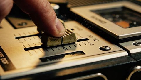 Sliding finger adjusting vintage cassette deck fader on dusty analog mixer close-up