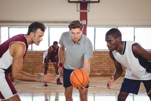 Basketball players are preparing for a jump ball in an indoor court, showcasing the intensity and focus of the game. This image is perfect for use in sports-related content, articles on teamwork and competition, or promotional materials for basketball events and training programs.