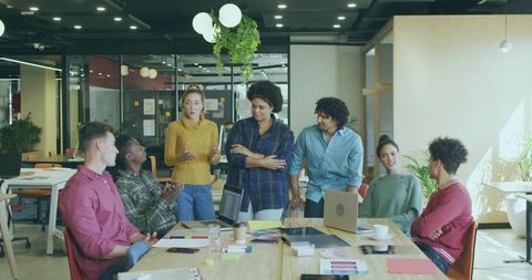 Diverse team brainstorming around collaborative table in modern co-working office with laptops