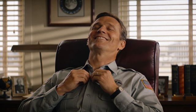 Smiling police officer in leather chair adjusting uniform collar, serene office moment