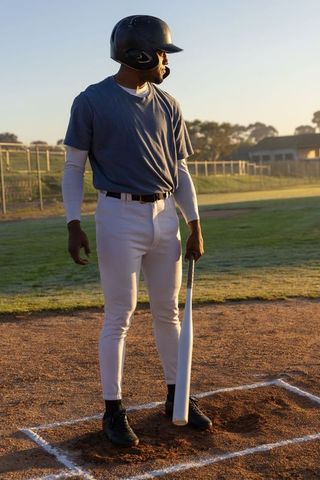 Adult male baseball player standing in batter's box holding bat at golden hour