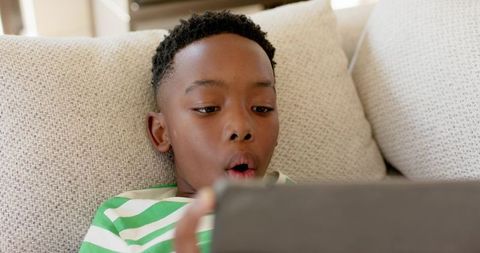 Young African American Boy Reacting to Tablet While Reclining on Beige Couch