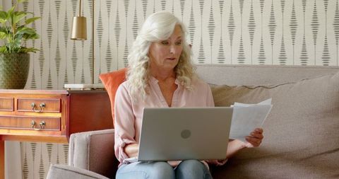 Mature Woman Concentrated Reviewing Documents on Laptop at Home