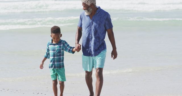 Happy senior african american father walking with son on sunny beach. healthy and active time beach holiday.