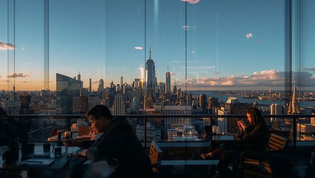 Rooftop bar overlooking nyc skyline at golden hour with guests enjoying glass reflections