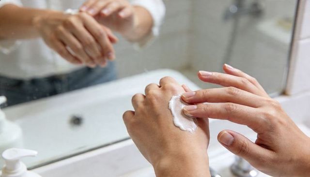 Applying moisturizer on hands at bathroom vanity mirror, daily skincare routine closeup