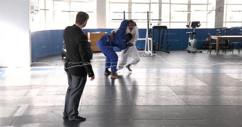 Instructor executing dynamic judo throw during martial arts training on padded mats in gym