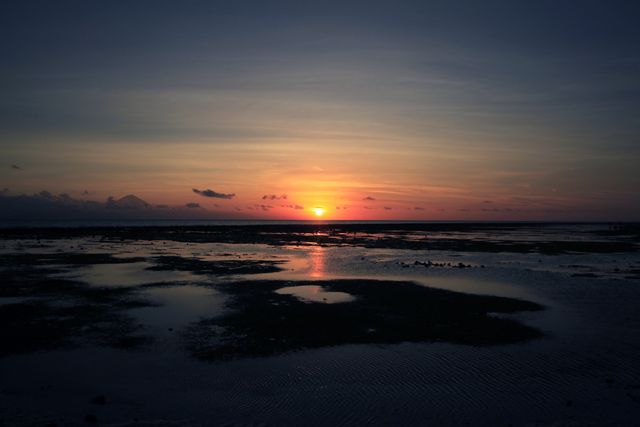 This beautiful image of a sunset over sandy tidal flats captures the serene and tranquil atmosphere of an evening by the coast. Ideal for use in travel blogs, nature photography collections, and inspirational content about relaxation and natural beauty.
