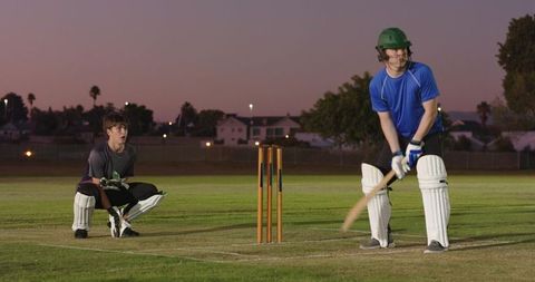 Evening cricket practice with batsman and wicketkeeper on suburban field at dusk