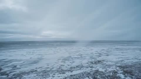 Shifting Frozen Shoreline Stretching Across Expansive Sea Under Moving Overcast Sky