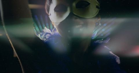 Posing masked woman wearing feather boa on dark stage with cinematic lens flare