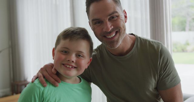 Portrait of caucasian father and son smiling in the living room at home. fatherhood and love concept